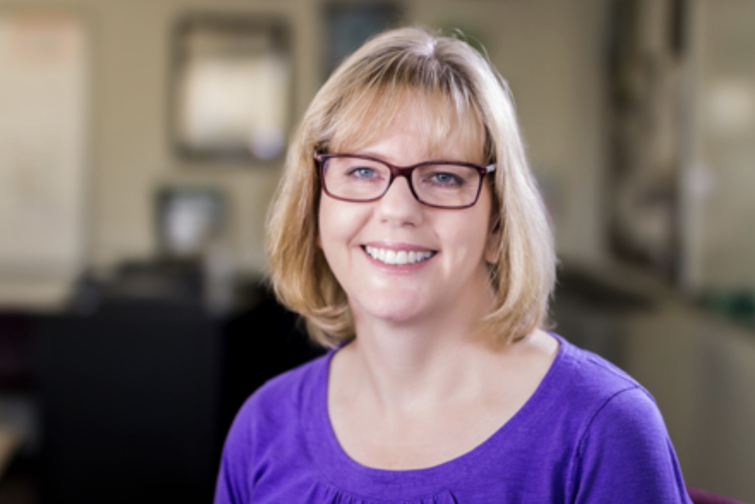 Blond smiling woman with purple shirt and glasses