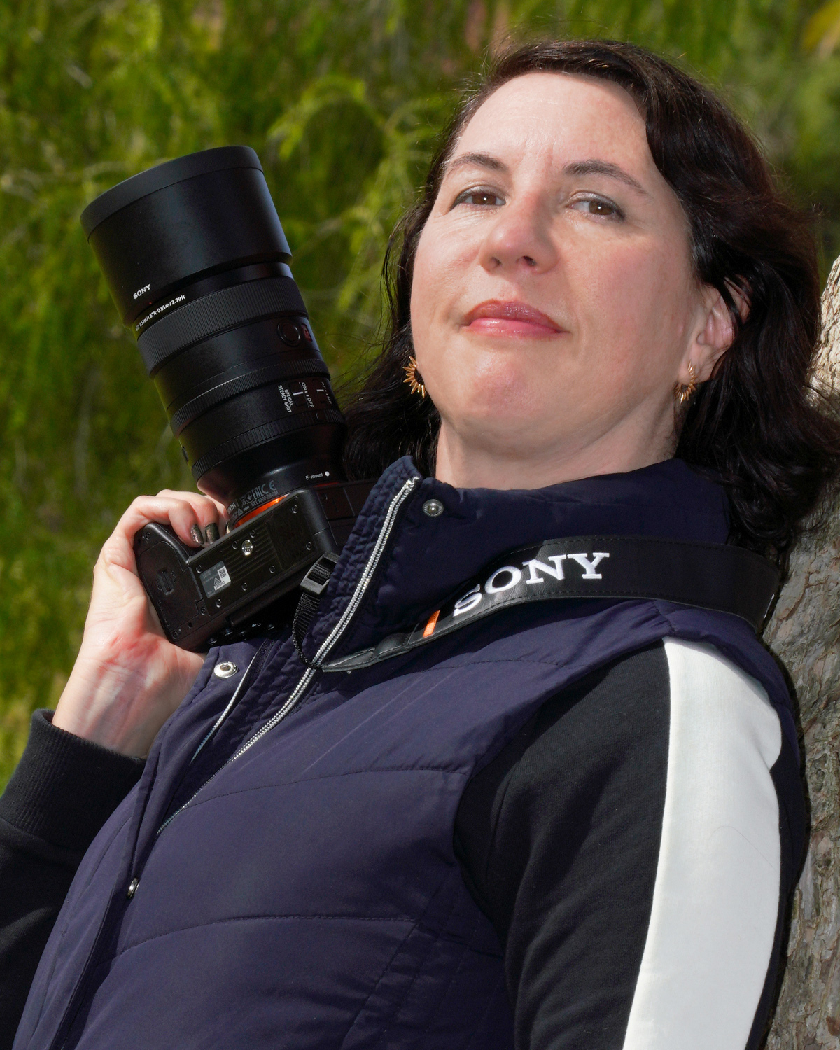Headshot photo of Instructor Amy Tierney holding a camera with attached lens in her right hand near her face 